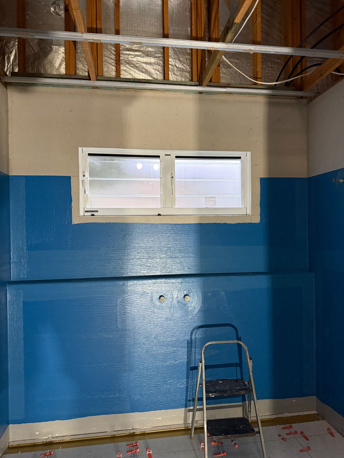 A bathroom stripped back to new sheeting with blue waterproofing membrane painted up the walls