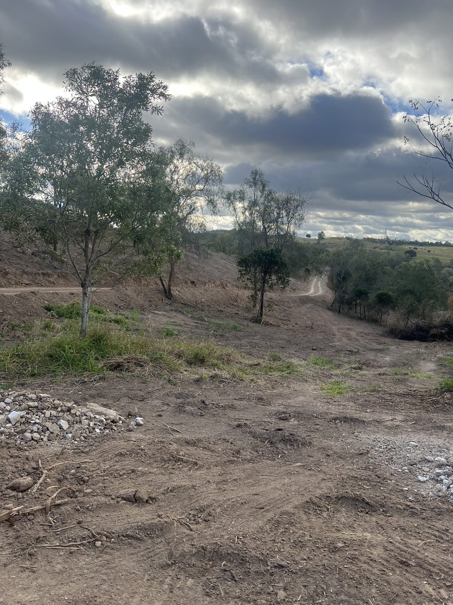 A cleared, levelled patch of dirt on a rural block with a gravel track running down through the trees behind