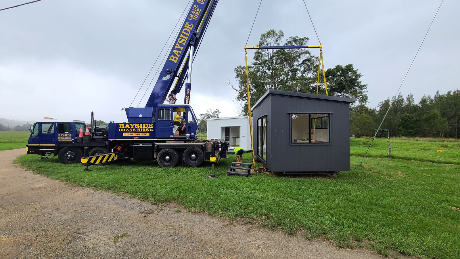 A crane lowering a dark modular home onto its spot in a paddock