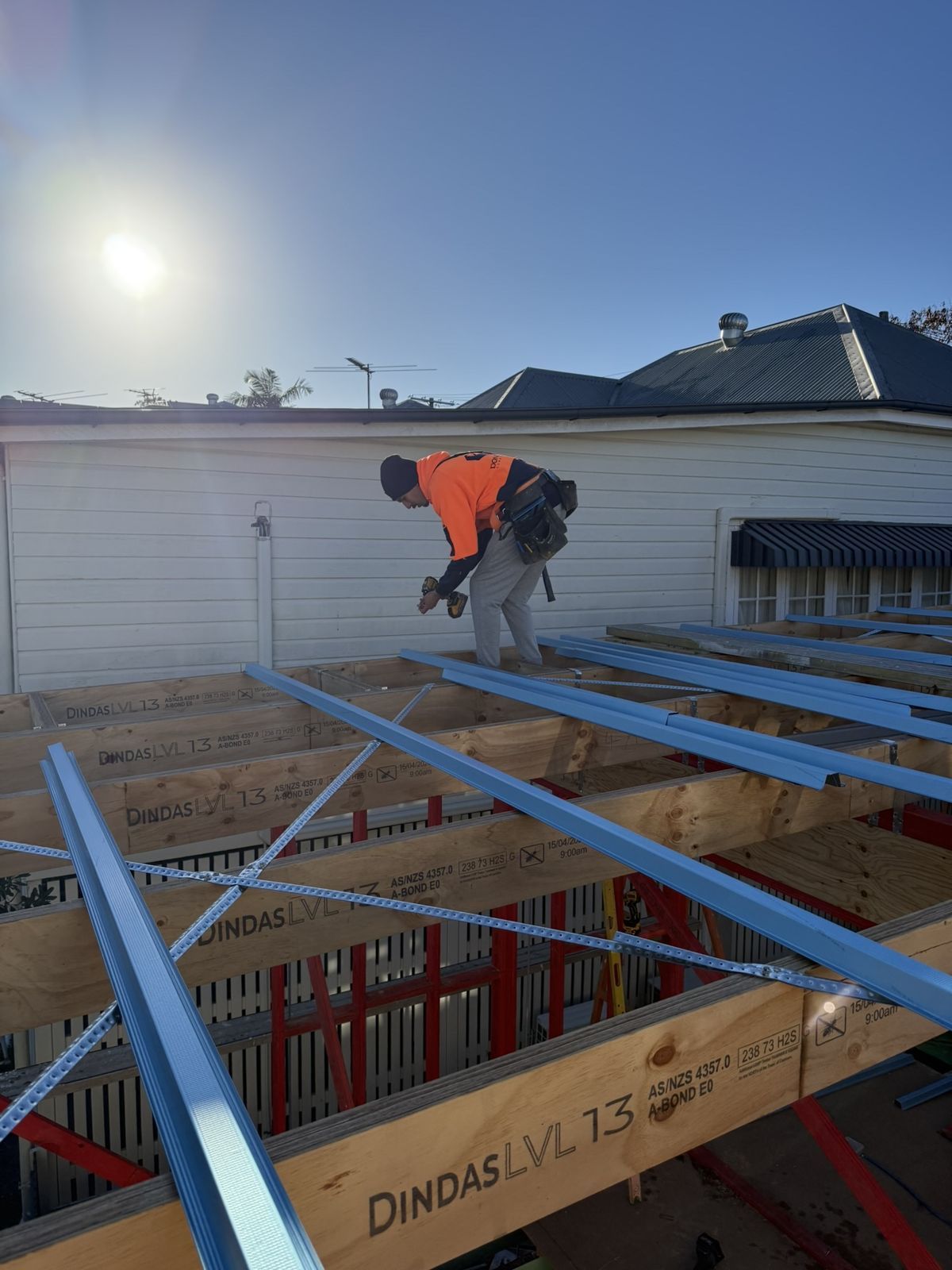 A roofer in hi-vis fixing steel roof battens over LVL rafters