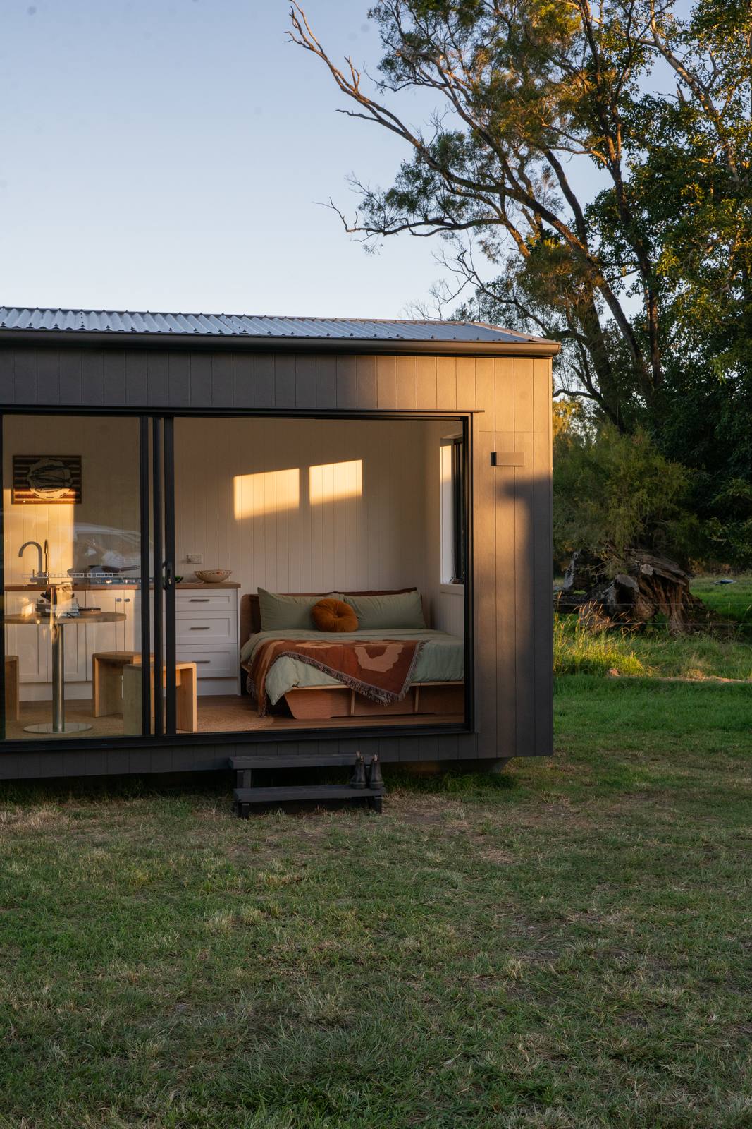 A dark-clad second home at golden hour, glass doors showing the bed and kitchen inside