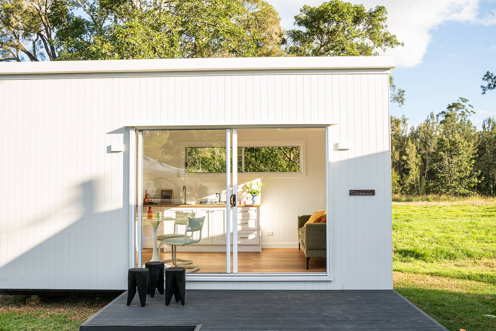 A white second home with its glass doors open onto a dark deck