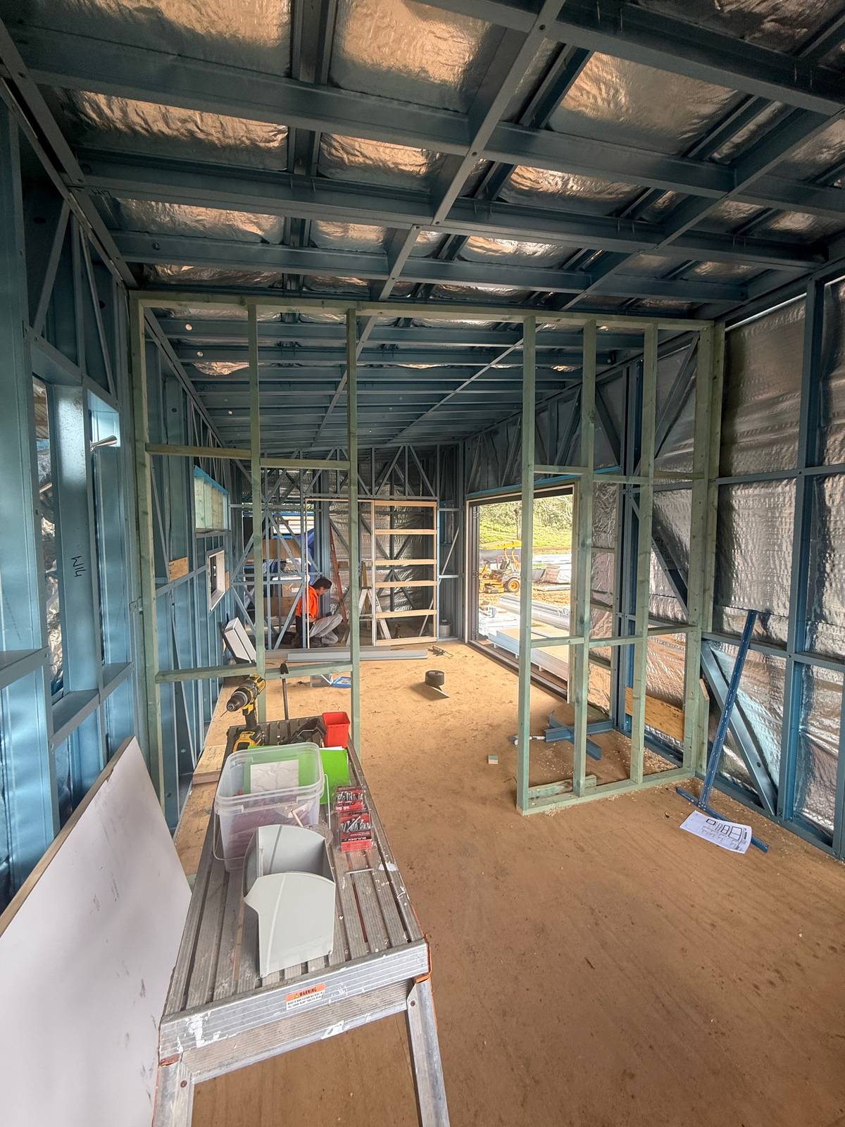 Inside a steel-framed module in the shed, foil-wrapped walls and ceiling, internal wall frames standing on a ply floor